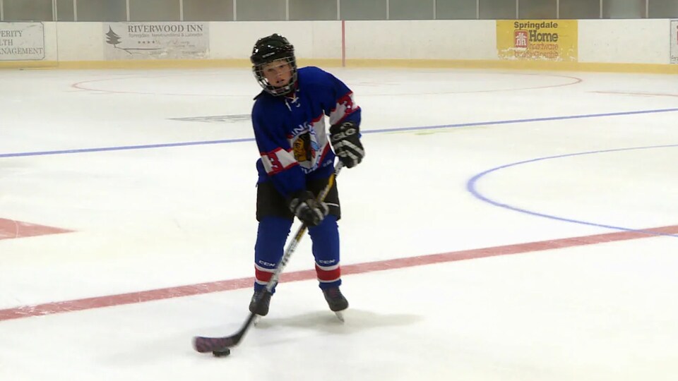 Le garçon en uniforme de joueur sur la patinoire d'un aréna.