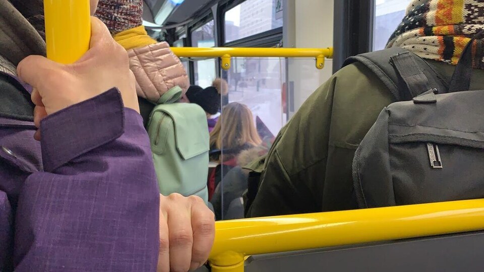 Des mains agrippent des barres à l'intérieur d'un autobus bondé.