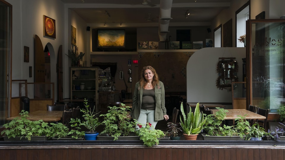 Portrait de Nina Djavanmard devant la grande fenêtre de son café où des plantes sont posées.