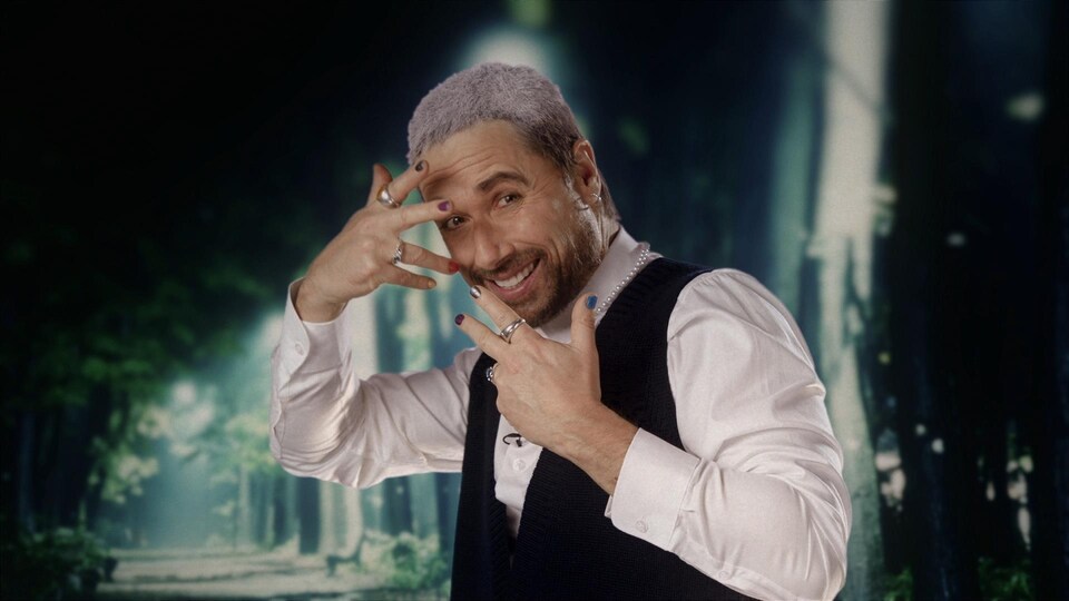 Stéphane Rousseau porte du vernis sur ses ongles et a le dessus des cheveux teint en blanc.