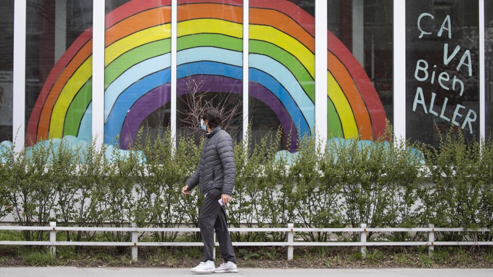 Un homme passe devant une fenêtre où est affiché un énorme dessin d'arc-en-ciel.