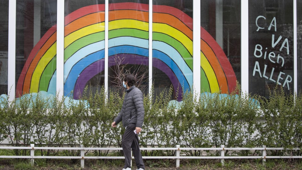 Un homme portant un masque passe près d'un grand arc-en-ciel collé à une vitrine.