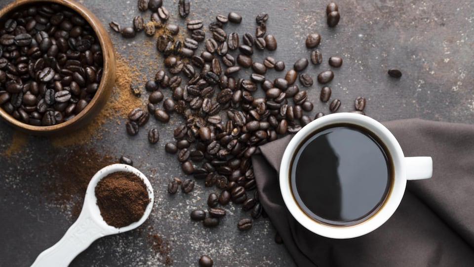 Du café torréfié, une tasse à café blanche avec du café noir, une serviette de couleur marron foncé avec une cuillère blanche remplie de café.