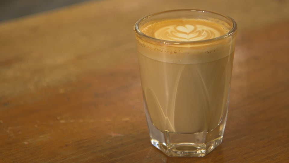 Un café latté dans un verre sur un comptoir de bois.
