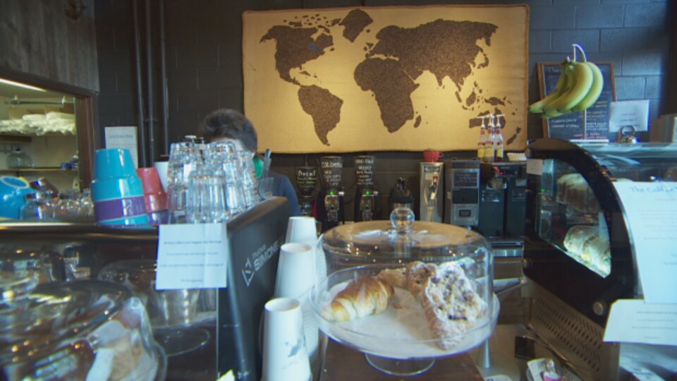 Photo prise dans un café. On y voit une carte du monde, des croissants sur le comptoir et une personne derrière une machine à café.