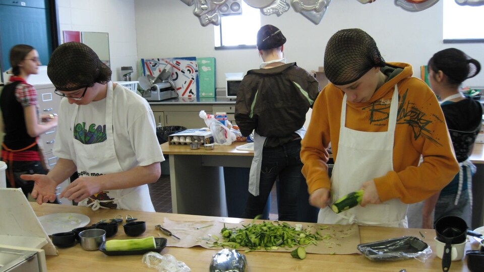Des jeunes s'affaires à préparer des légumes dans une cuisine d'une école secondaire.