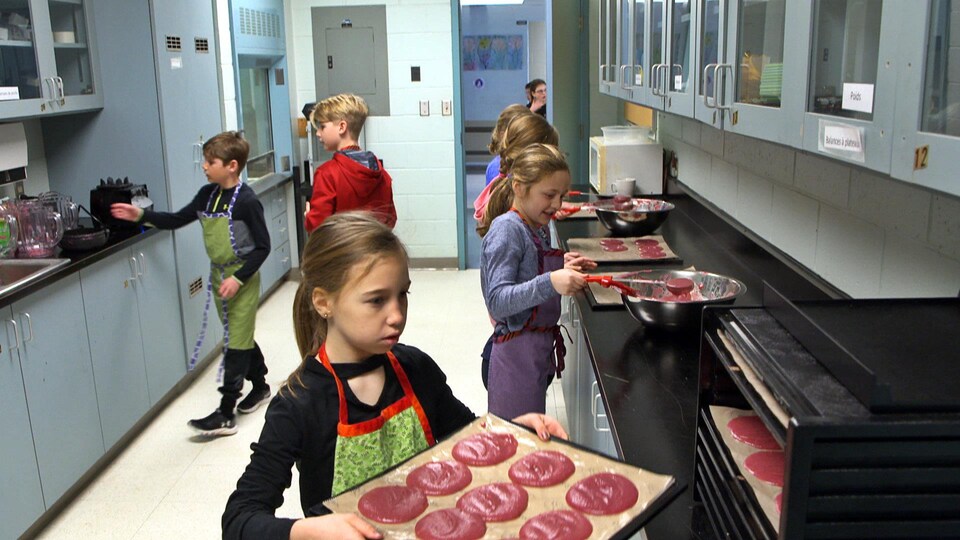 Des enfants préparent des roulés aux fruits dans une cuisine.