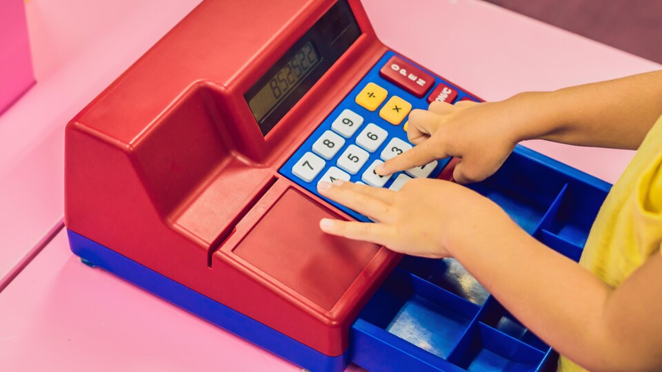 Les mains d'une enfant qui joue avec une caisse enregistreuse.
