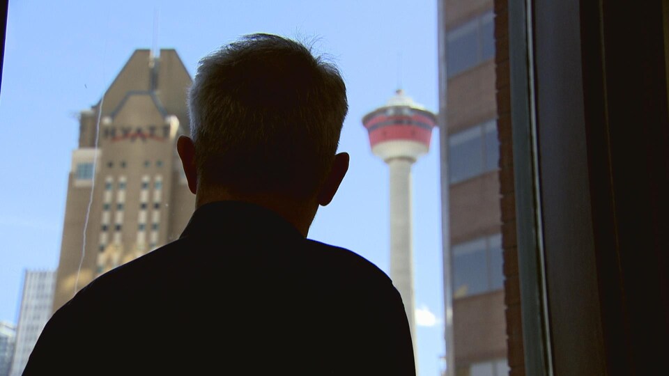 Un homme regarde par la fenêtre en direction de la tour de Calgary.