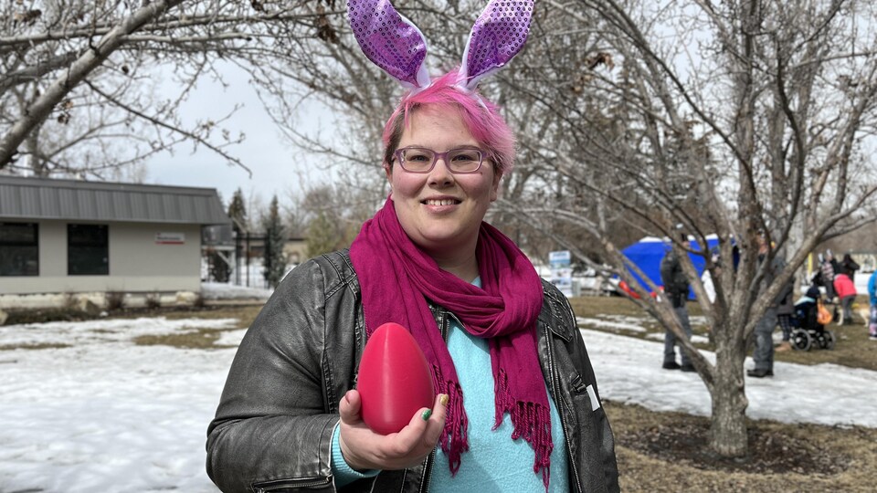 Une personne portant des oreilles de lapin et tenant un œuf de Pâques sourit.