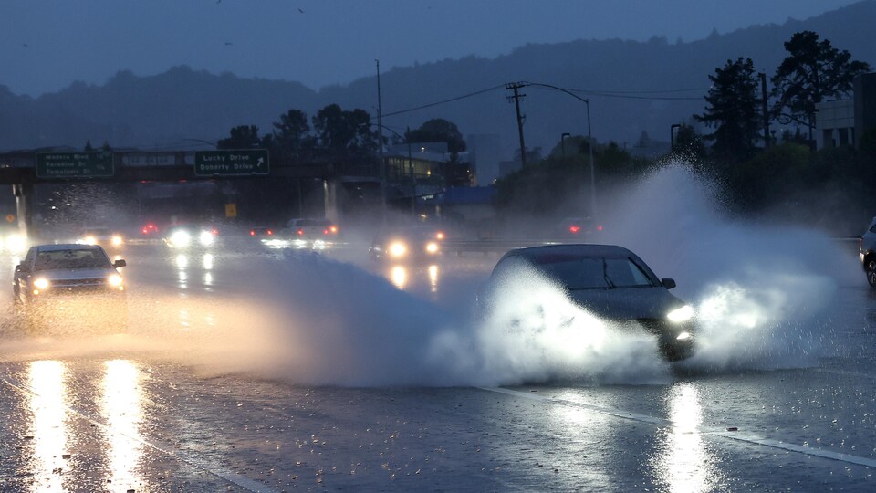 Une voiture soulève des trombes d'eau en circulant sur la route.