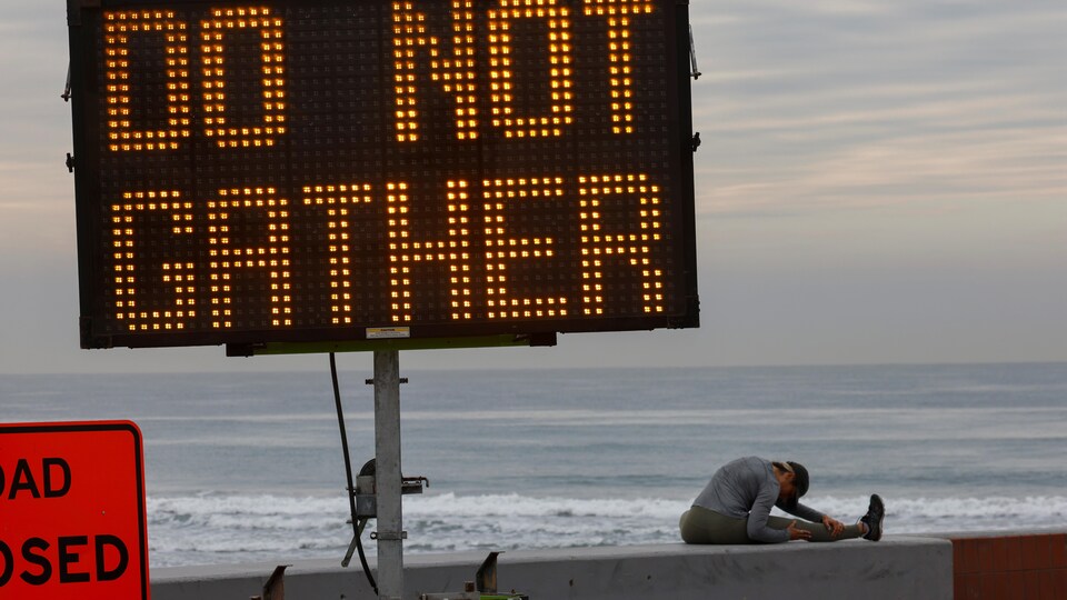 Une femme s'étire près d'un panneau qui interdit les rassemblements à la plage en Californie.