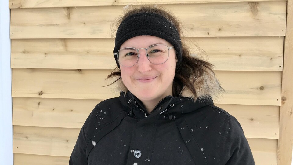 Une jeune femme porte un bandeau et des lunettes pour la vue. Elle porte aussi un manteau et il neige à l'extérieur. 