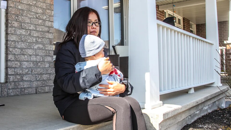 A woman sitting on the balcony of her house holding a baby in her arms.