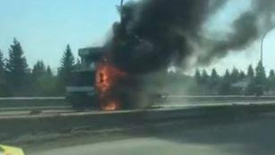 Un camion en feu sur la route, une fumée épaisse s'en échappe.