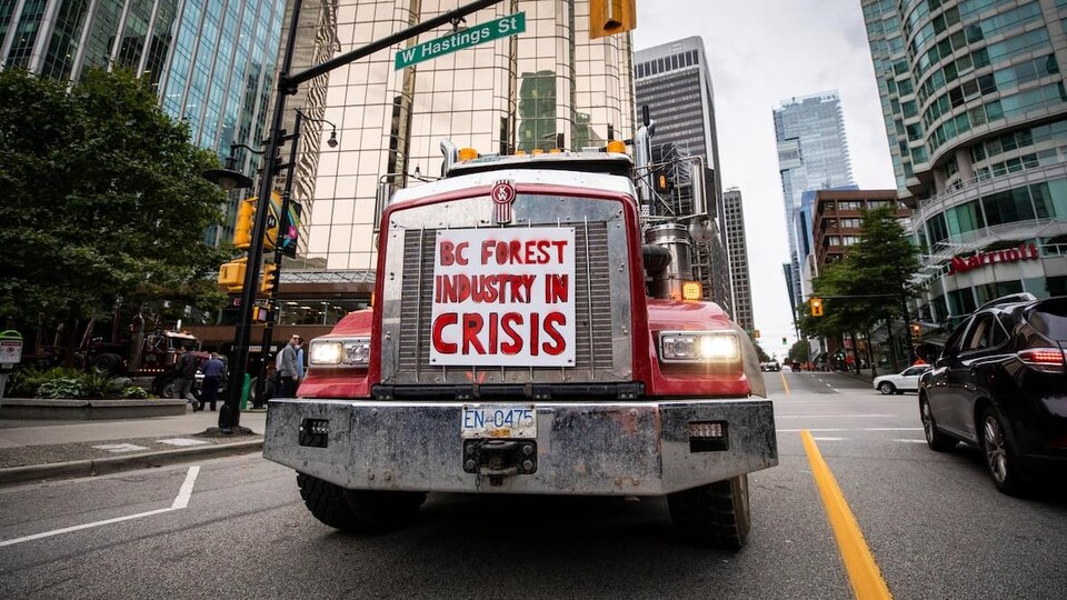 Une affiche où il est écrit en anglais : « L'industrie forestière de la Colombie-Britannique en crise » est posée sur la grille avant d'un camion lourd qui roule dans les rues de Vancouver.