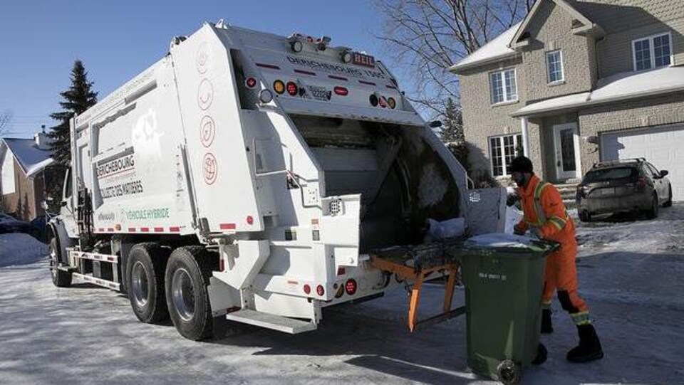 Un éboueur est en train de vider un bac à ordures à Gatineau.