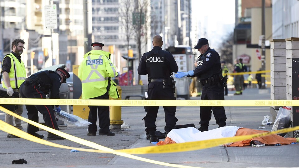 Des policiers torontois recueillent des objets près du corps d'une des victimes.