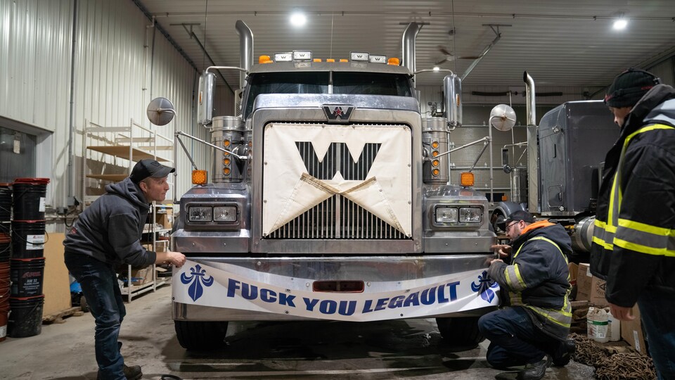 Deux camionneurs installent une banderole sur un camion. 