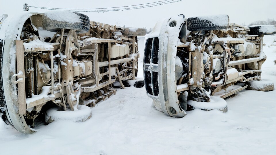 Deux camions sont sur le côté dans la neige avec le dessous du véhicule exposé.