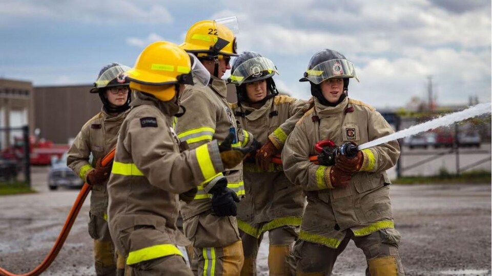 Des jeunes femmes tiennent un boyau d'arrosage de pompiers.