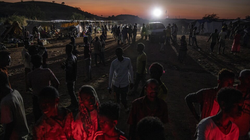 Des dizaines de personnes se promènent dans le camp alors que la nuit tombe.