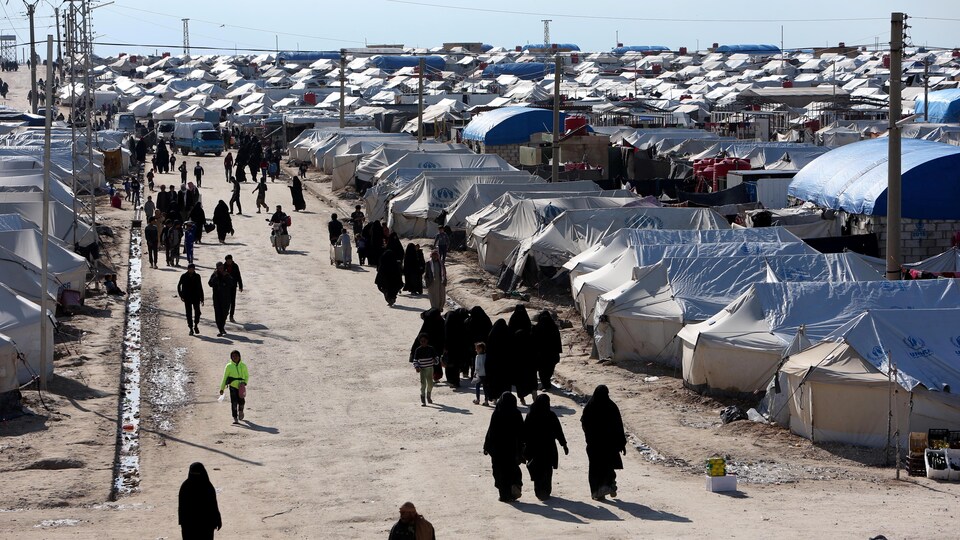 De nombreuses tentes blanches et des gens, dont des femmes couvertes de la tête au pied, marchent dans une allée. 