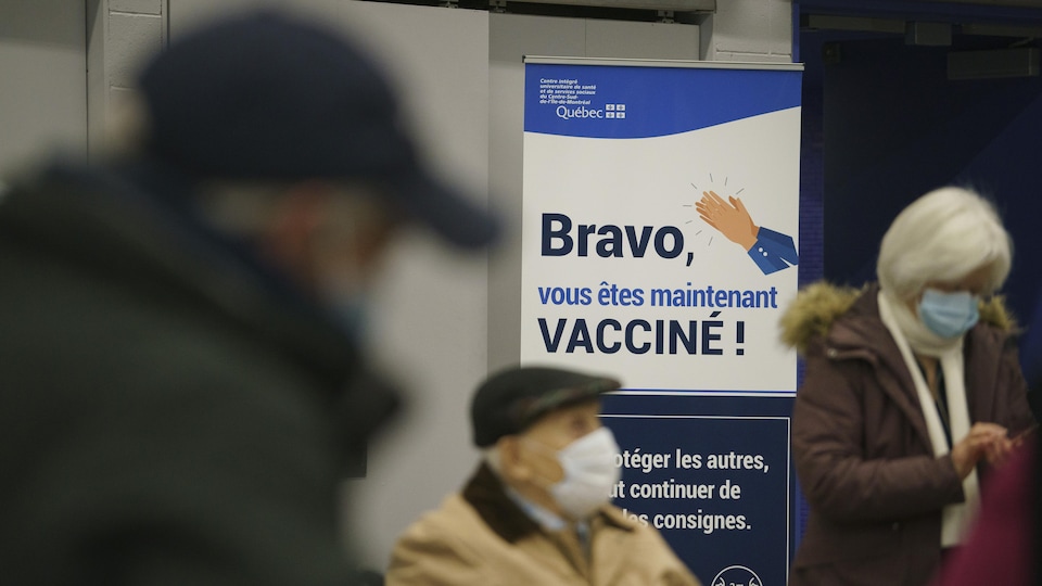 Trois personnes attendent près d'une pancarte où on peut lire : « Bravo, vous êtes maintenant vacciné! »