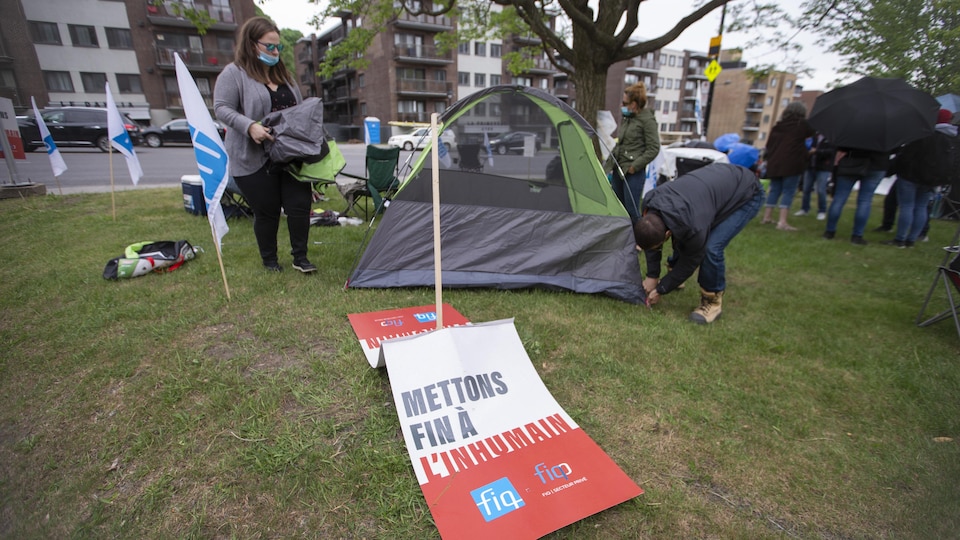 Deux personnes installent une tente devant une pancarte sur laquelle est écrit : «Mettons fin à l'inhumain».