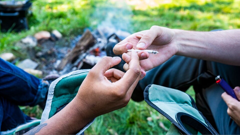 Des gens s'échangent un joint devant un feu de camp.