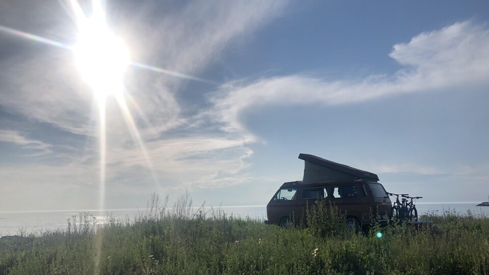 Une Westfalia stationnée dans un espace vague, près du bord de l'eau.