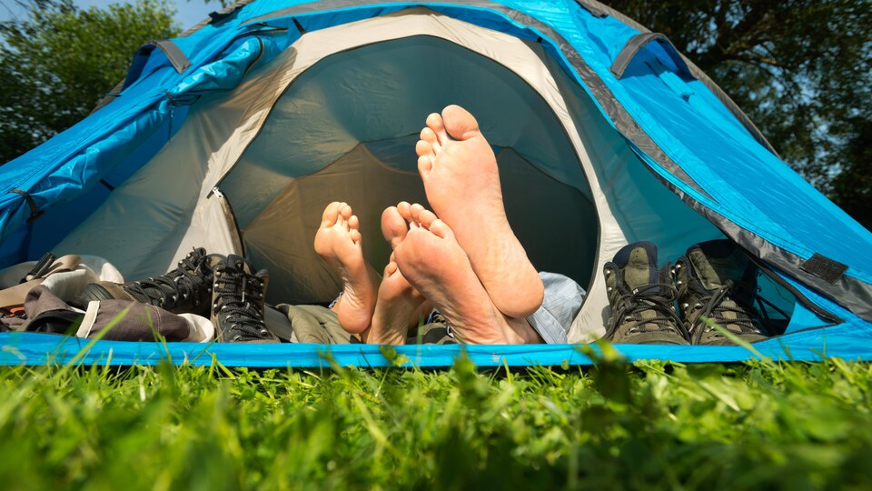 Une tente est ouverte. On voit les pieds de deux personnes qui sont couchées à l'intérieur. Leurs chaussures se trouvent près de la porte.