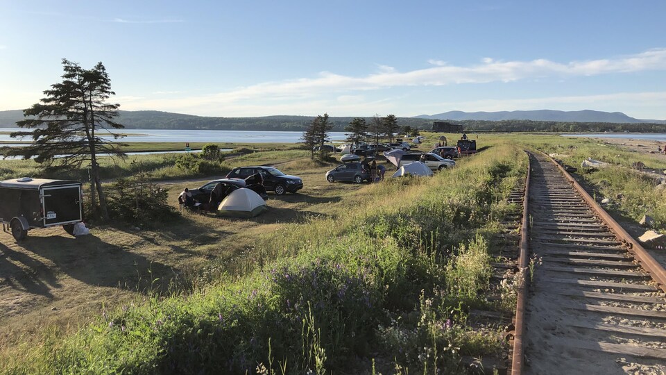 Des véhicules et des tentes sont installés entre une plage et un chemin de fer à Douglastown, en Gaspésie.