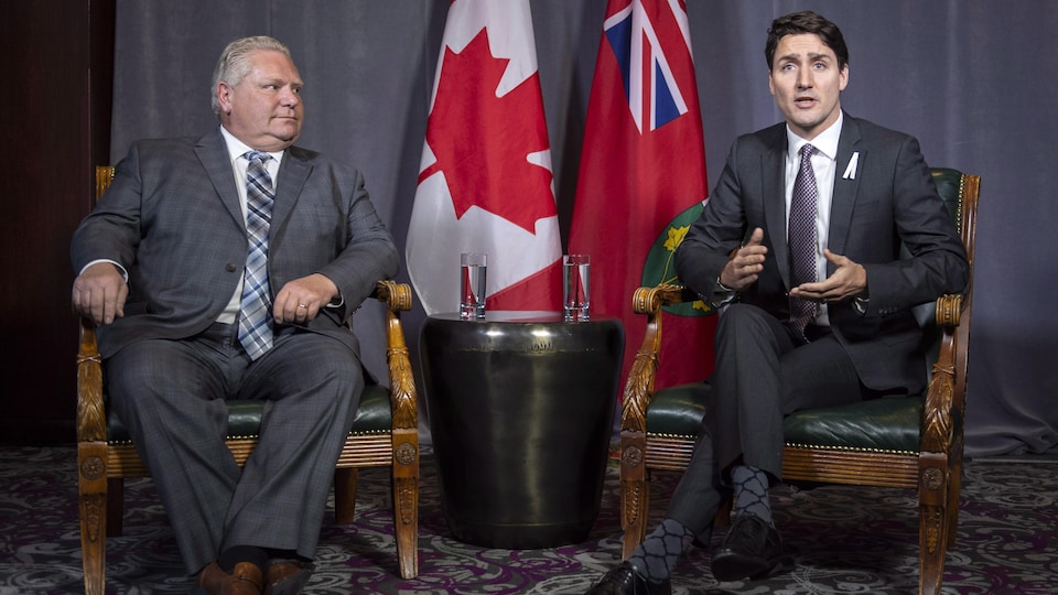 Doug Ford et Justin Trudeau, assis sur des fauteuils, répondent aux questions des médias devant les drapeaux canadien et ontarien.