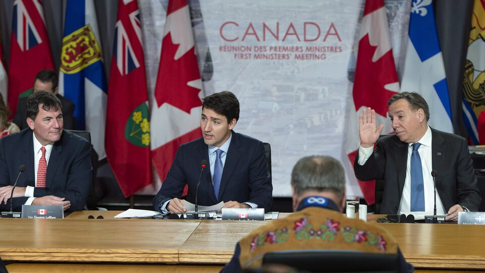 Dominic LeBlanc, Justin Trudeau and Francois Legault sat at a table, in front of the flags of Canada and the provinces.