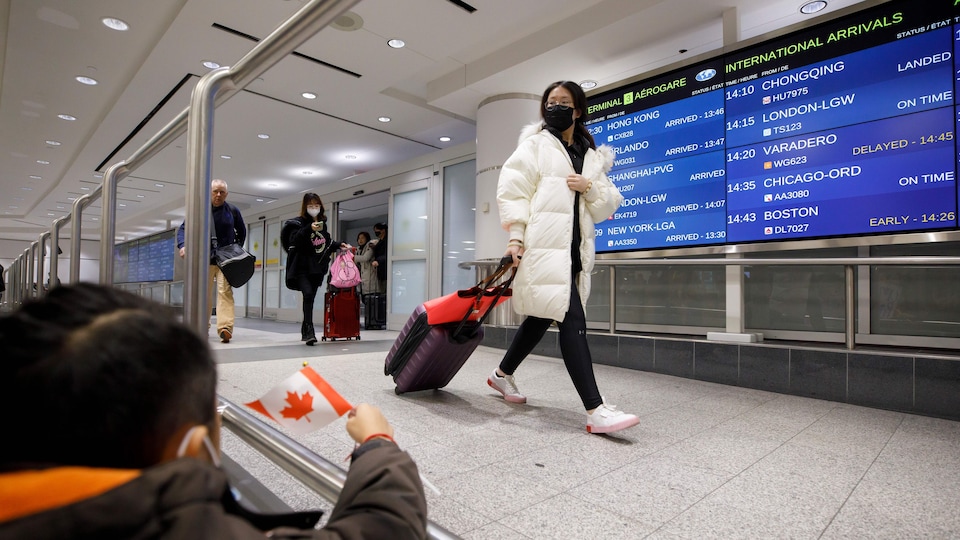 Une voyageuse porte un masque et tire sa valise.
