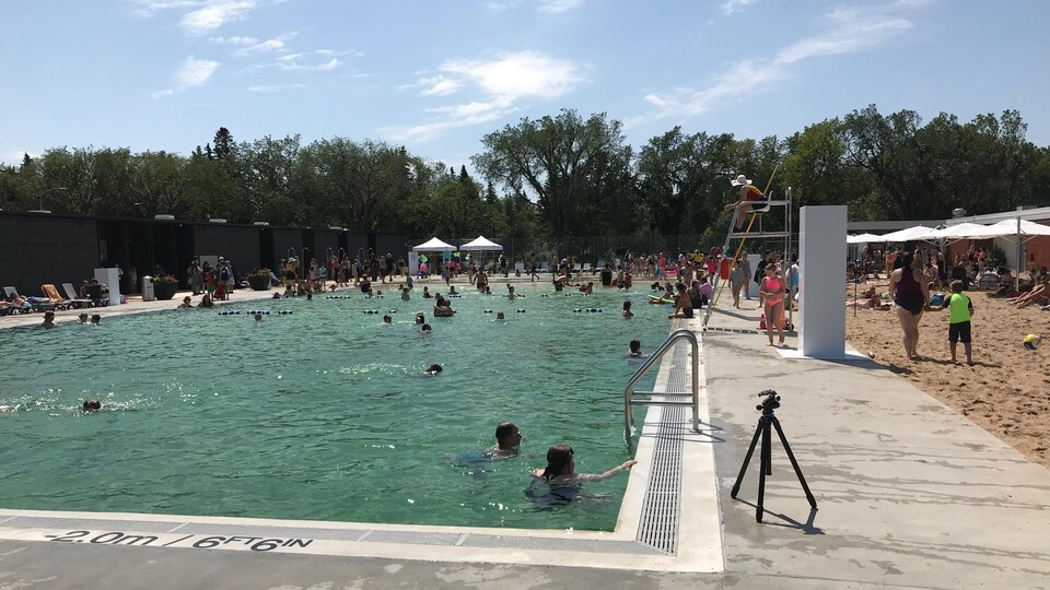 Dans l'image, il y a une partie de la piscine et du terrain de volley-ball. Des gens se baignent dans la piscine.