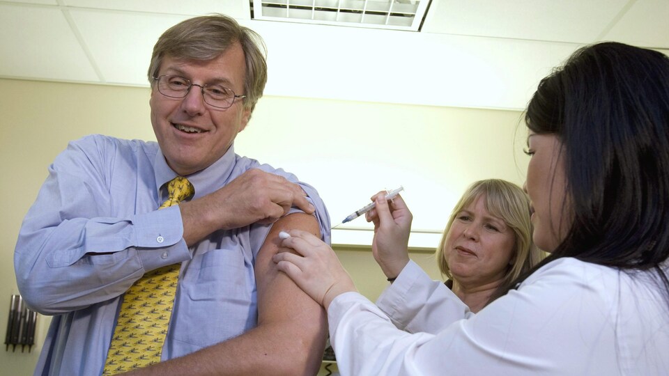 Une infirmière administre un vaccin à un homme dans la soixantaine.