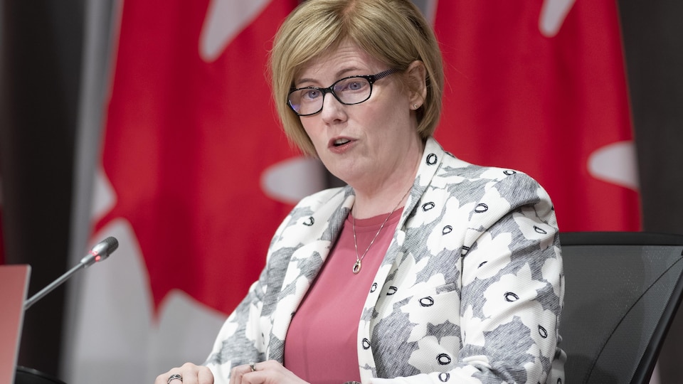 La ministre Qualtrough lors d'une conférence de presse à Ottawa, avec le drapeau canadien visible en arrière-plan.
