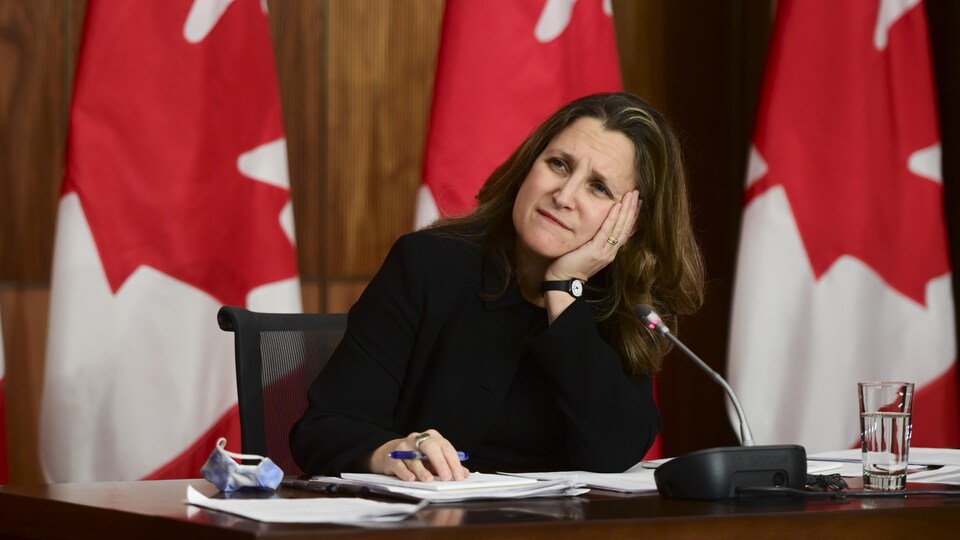 Assise à un bureau la tête appuyée dans la paume de sa main, Chrystia Freeland écoute la question d'un journaliste.