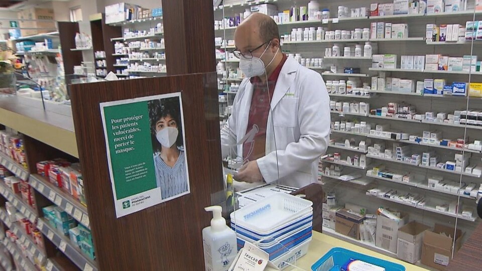 Un pharmacien manipule des médicaments devant un étalage de boîtes et de flacons.