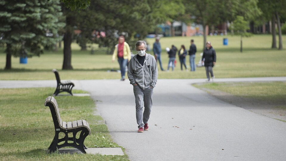Un homme portant un masque de protection marche dans un parc.