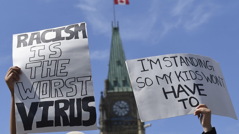 Deux personnes tiennent des pancartes devant le parlement à Ottawa.