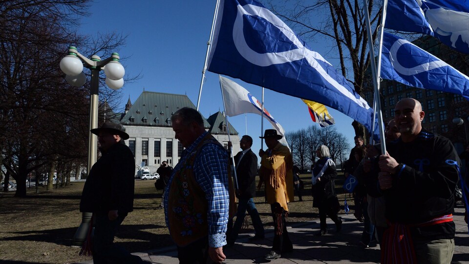 Le président de la Fédération des Métis du Manitoba, David Chartrand (milieu), marche avec le drapeau métis devant la Cour suprême du Canada.