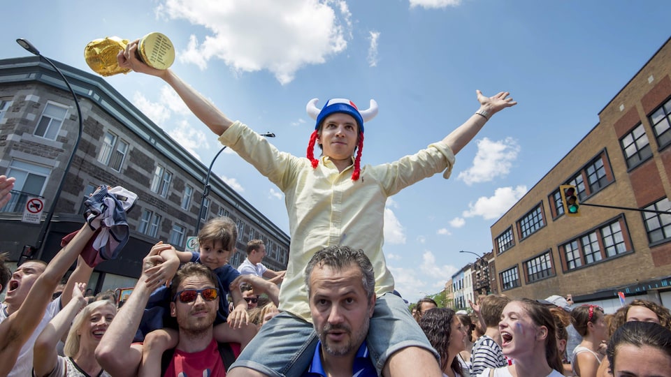 Un homme portant une coupe et un chapeau de gaulois sur les épaules d'un autre homme au milieu d'une foule