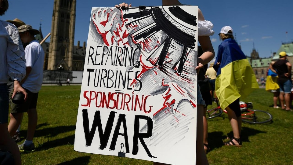 Eine Frau hält eine Tafel mit einer Botschaft "Turbinen reparieren, den Krieg finanzieren".