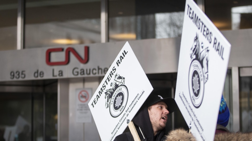Deux personnes tiennent des pancartes du syndicat des Teamsters devant les bureaux du CN.