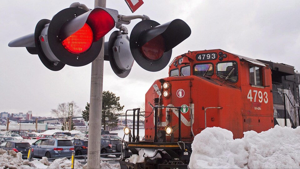 Une locomotive du CN à l'arrêt devant un feu de circulation de voie ferrée à proximité d'un stationnement de voitures.