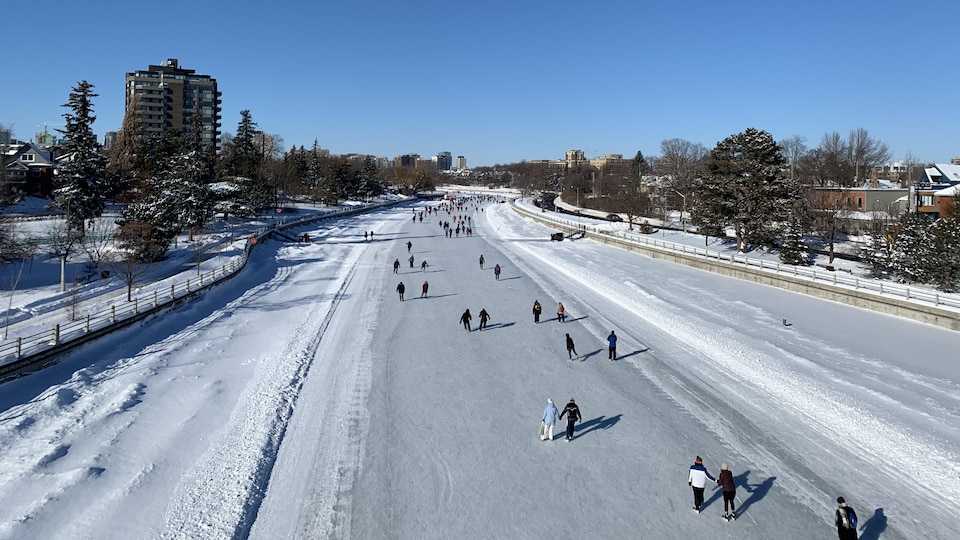 Vue du canal Rideau d'Ottawa en hiver depuis un pont avec plusieurs dizaines de patineurs sur la glace.