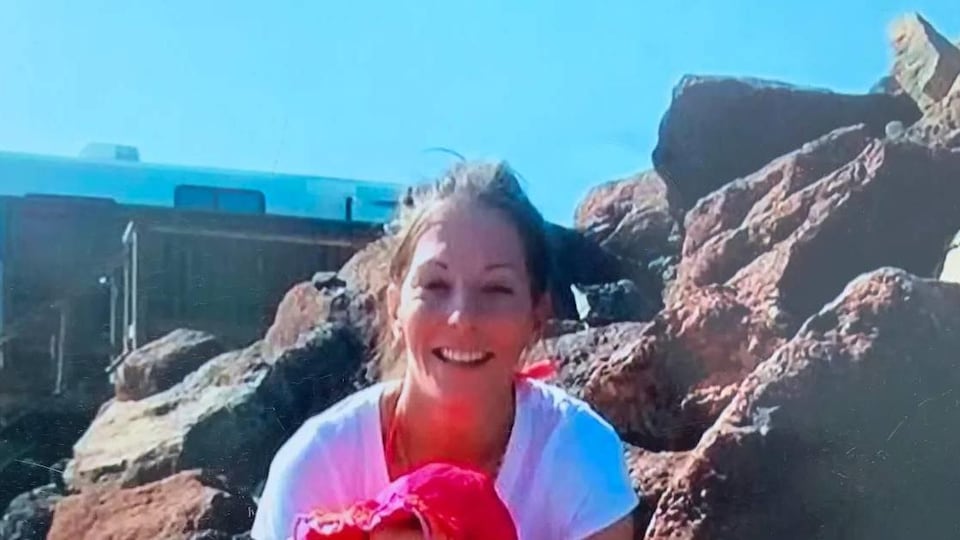 Une femme souriante assise sur des rochers.